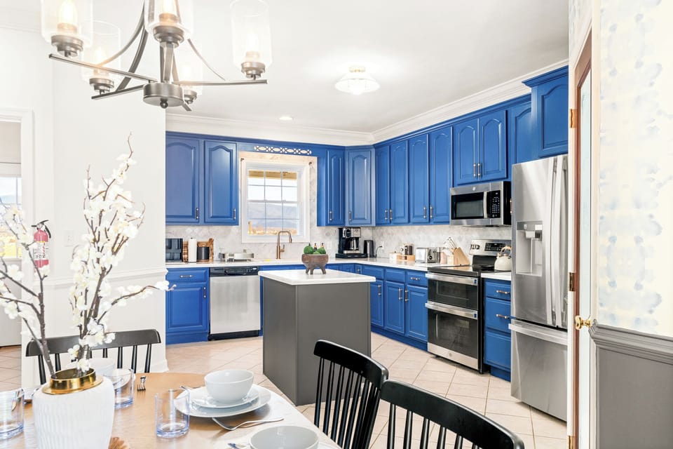 Vibrant blue kitchen with stainless appliances, spacious island, and ample counter space—fully equipped for family breakfasts, holiday baking, and casual coffee chat.