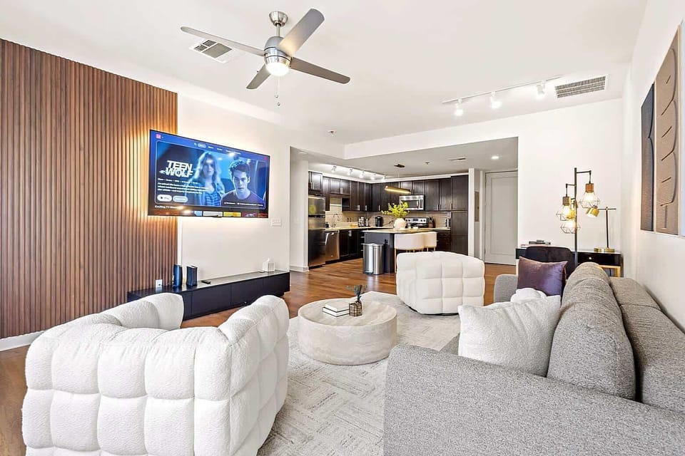 Modern open concept living area featuring a 75 inch Smart TV, plush sofas, and warm decor. Ideal for movie nights, lounging, and spending quality time together.