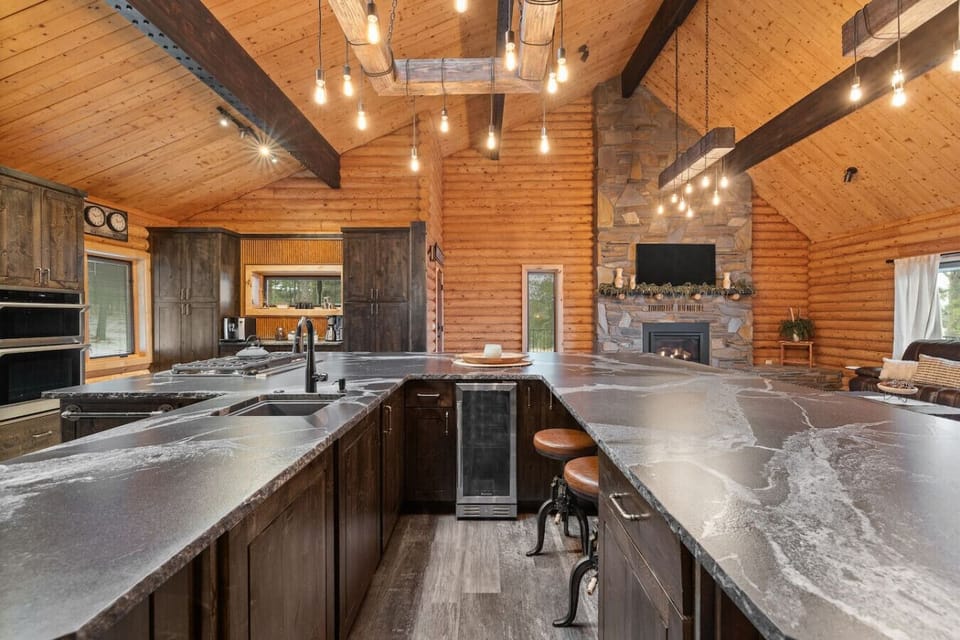 Experience the perfect blend of modern luxury and cozy cabin charm in this stunning, fully-equipped kitchen, featuring high vaulted wood ceilings and exposed dark beams.