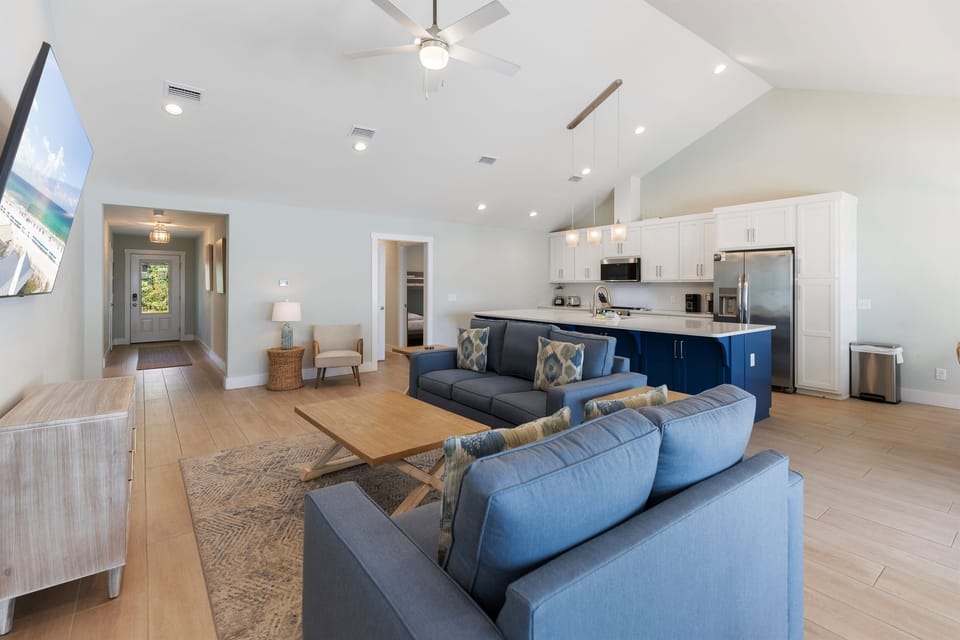 Relax in your spacious open-concept living space with vaulted ceilings, modern blue sectional, and fully equipped kitchen perfect for your getaway.