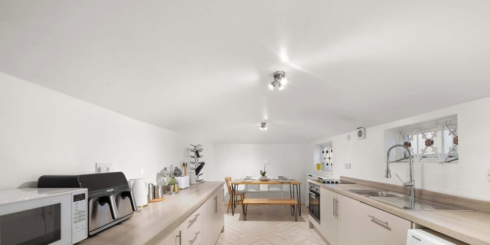 Modern galley kitchen featuring light wood counters, white cabinets, and herringbone flooring. A simple wooden dining set is tucked into the far end.
