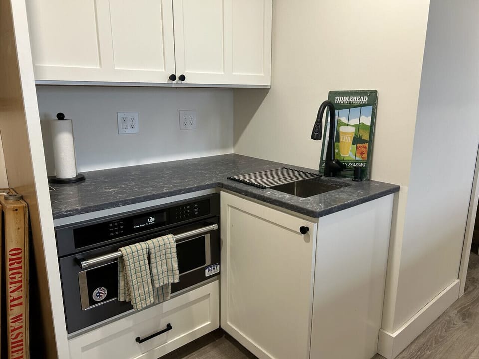 Located for easy access, this handy wet bar features dark countertops, a built-in microwave, and a small sink.