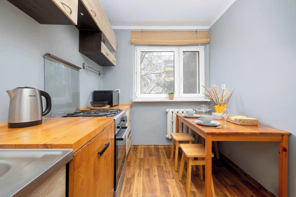 Another view of the same kitchen showing the wooden cabinets and window. The dining table is neatly arranged and ready for use.