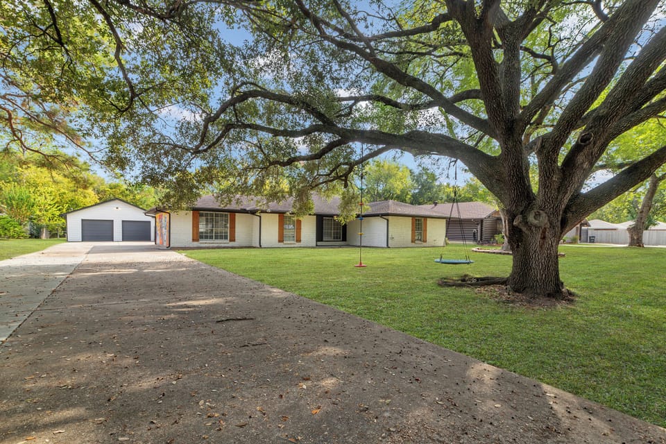 Peaceful front yard with wide driveway, shady tree, swing, and 2-car garage!