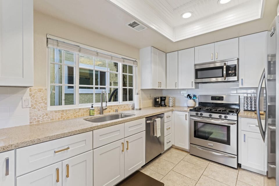 Light-filled kitchen w/ white cabinetry, modern appliances & window views