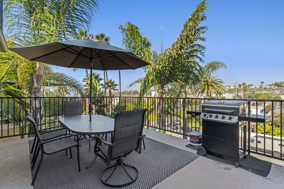 Balcony dining setup w/ umbrella, grill & leafy views for easy outdoor meals