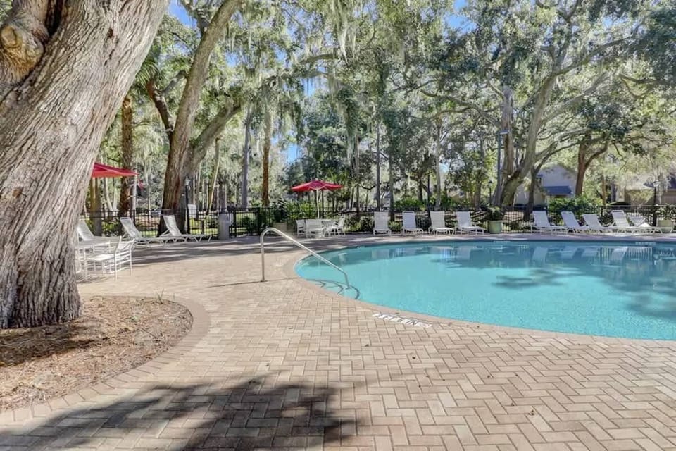 Relax by the outdoor pool surrounded by mature trees and lounge chairs.