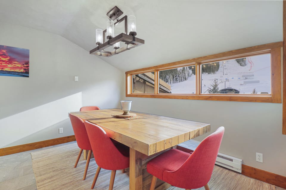 Gather around this stunning reclaimed wood dining table where you'll share memorable meals with mountain views as your backdrop. The warm coral chairs and rustic chandelier create the perfect ambiance for your alpine getaway.