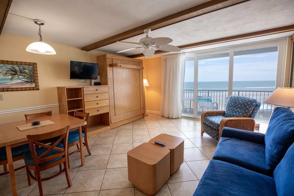 This inviting oceanfront studio features a cozy living area with a queen Murphy bed, a comfortable sofa bed, and a charming dining space, all bathed in natural light from the sliding doors leading to the private balcony.