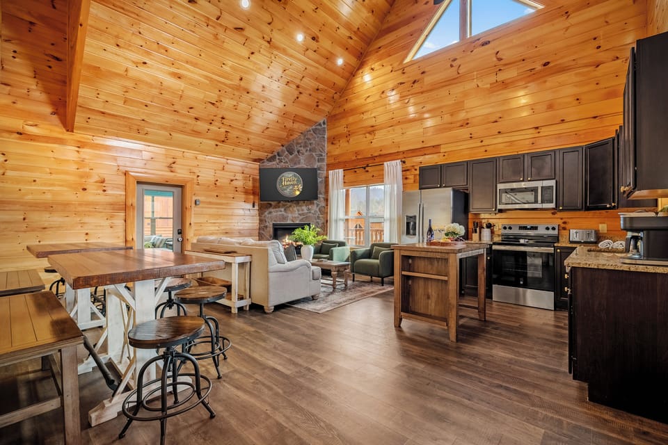 Vaulted pine cabin great room with stone fireplace and sleek, stainless kitchen.