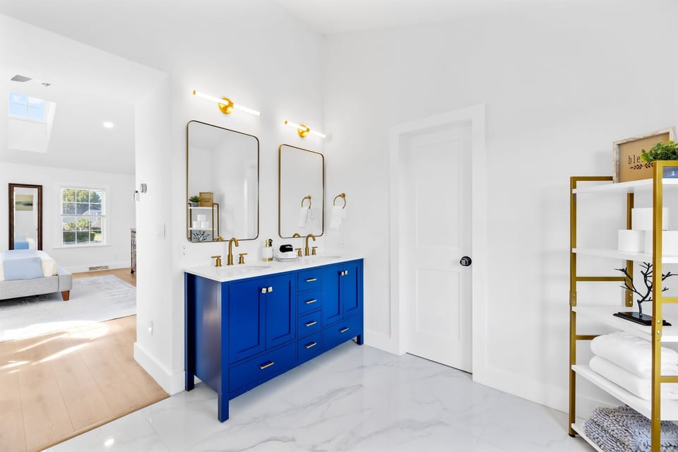 Primary full bathroom with a blue double vanity, gold-accent mirrors and shelving.