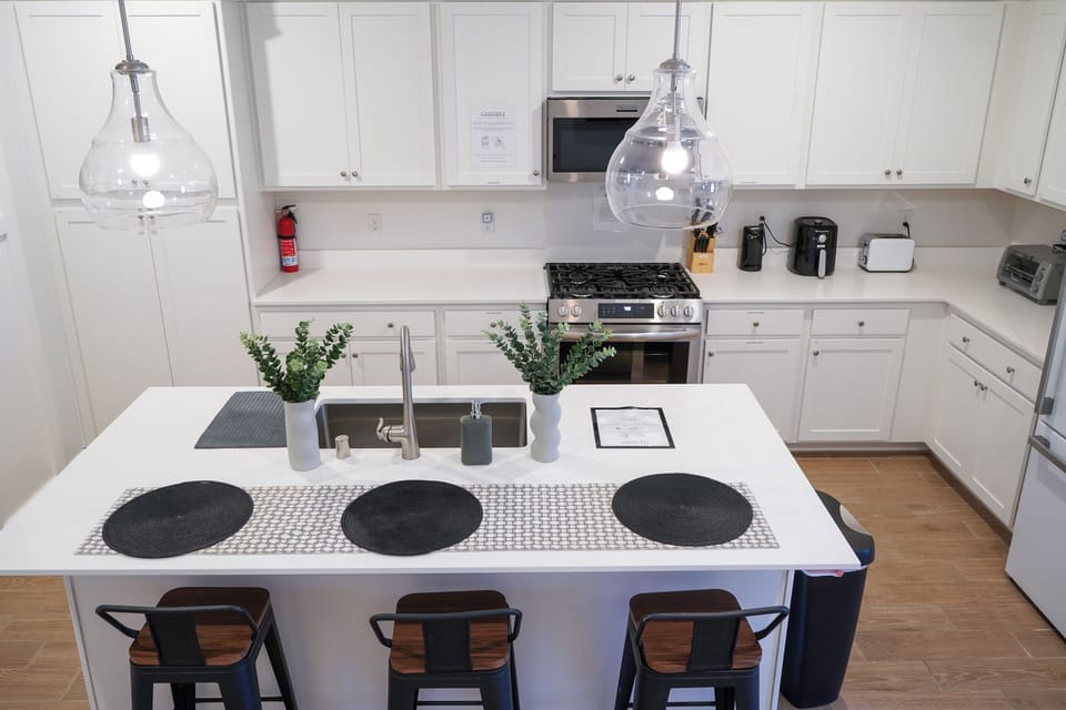 Bright white kitchen with island, brown barstools, modern appliances, and plants