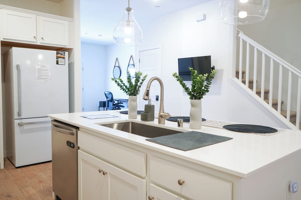 Bright white kitchen with large island, modern fridge, and greenery.