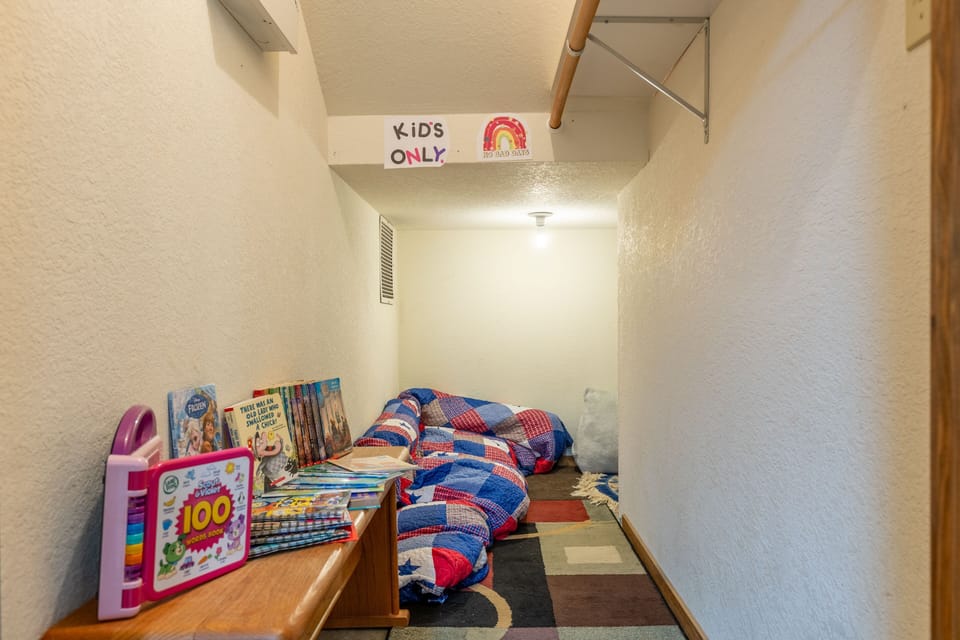 A small kids' play nook set under the stairs with books, bedding, and a colorful rug.