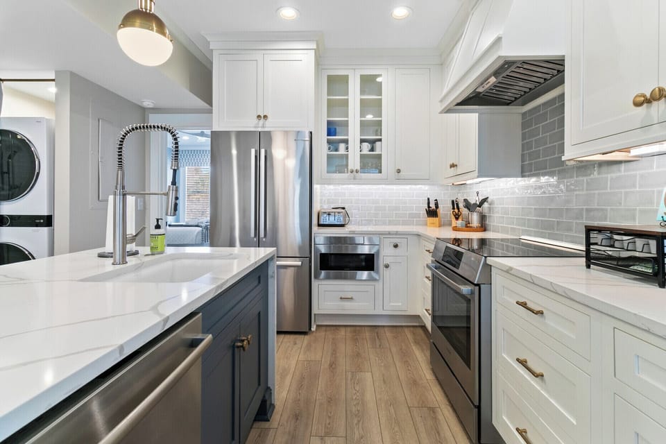 Shaker-style cabinetry, stainless steel appliances, and soft gray tile create a bright, polished kitchen with timeless seaside charm.