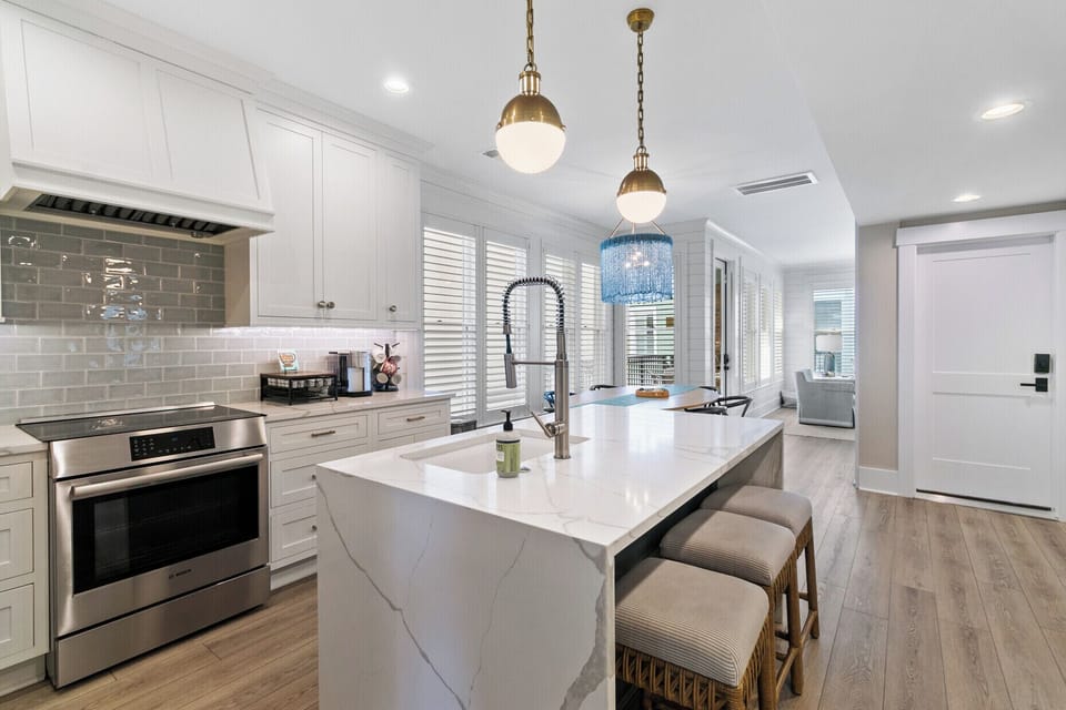 A sleek white island, brass accents, and soft blue lighting create a fresh and inviting space perfect for gathering and entertaining.