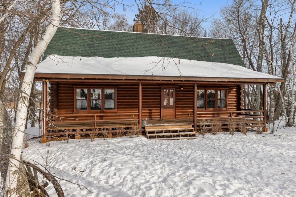 Handcrafted log cabin on the Whitefish Chain of Lakes, featuring a covered porch and rich wood detailing. An exceptional lakefront setting that pairs classic log architecture with a professionally designed interior. (before photo)