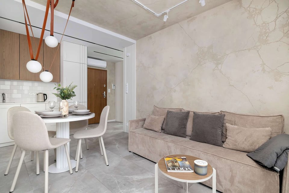 A stylish living area featuring a sofa, a round dining table, and elegant lighting. The space is designed for both relaxation and shared meals.