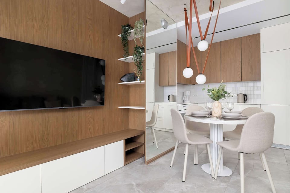A dining area combined with a media wall, featuring a wall-mounted TV and a round table. The layout encourages both dining and evening relaxation.