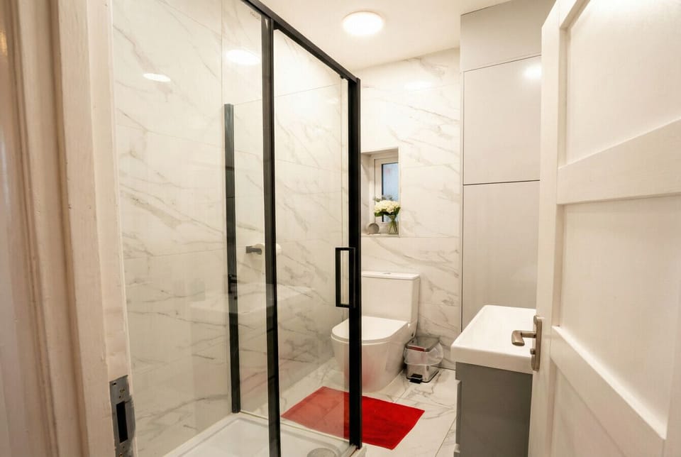 The shower room features floor-to-ceiling marble-effect tiles, a glass-panelled walk-in shower enclosure, a wall-hung basin, and a WC.