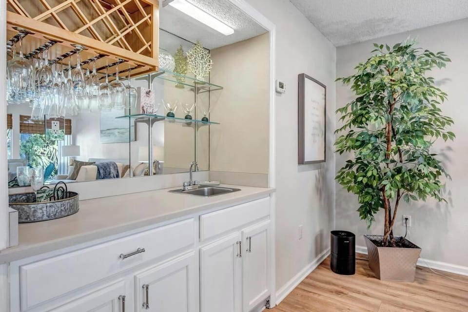 Stylish wet bar w/ hanging wine glasses, sleek sink, and a large mirror that brightens the space.