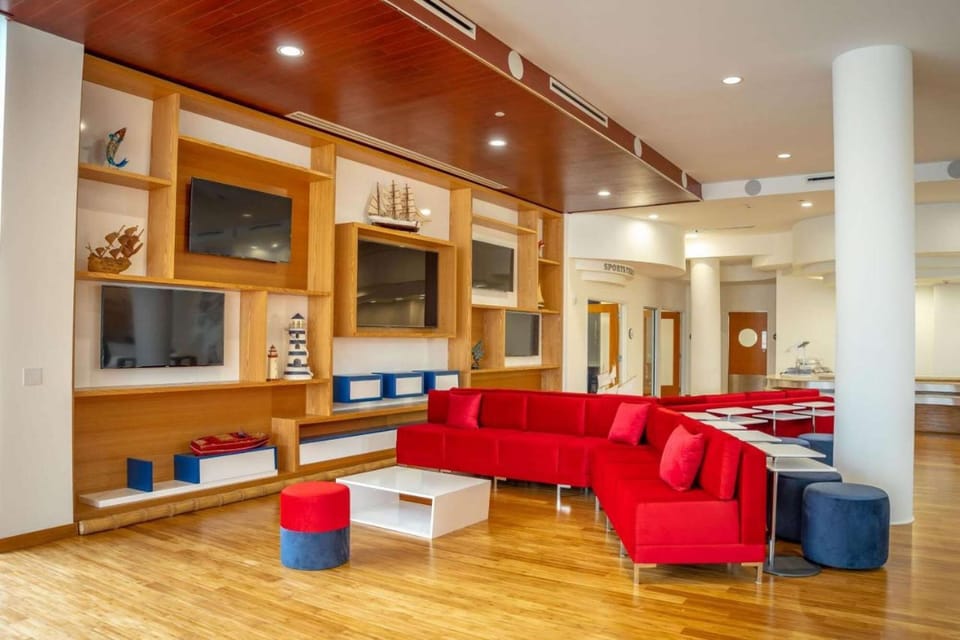 Cozy lounge with red sofa, stools, and TVs on wooden shelves.