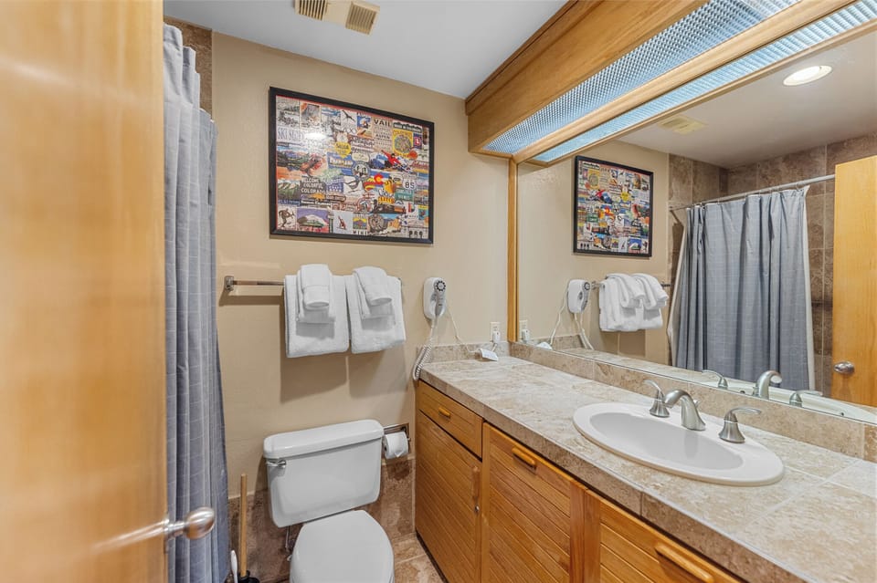 Your private bathroom features a spacious vanity with ample storage, modern fixtures, and thoughtful touches like fresh towels and unique wall art.