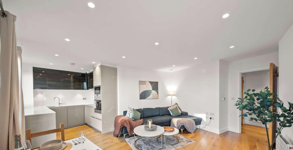 This bright, open-concept apartment features warm wood floors and an integrated living and kitchen space. Modern furnishings, including a dark sofa and round coffee tables, create a clean and inviting atmosphere.