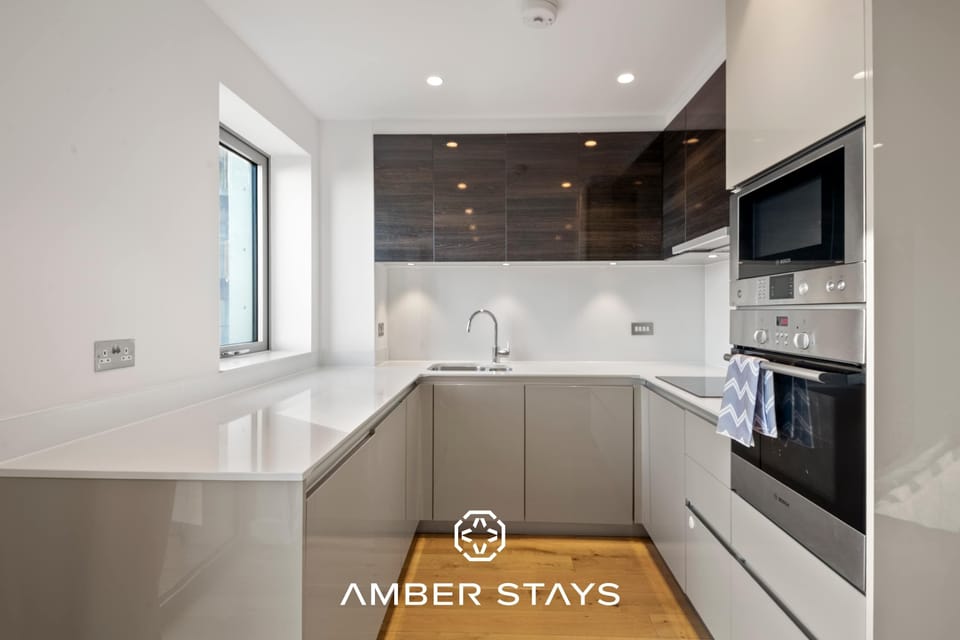 This modern U-shaped kitchen features a sleek, minimalist design with glossy white countertops and two-toned cabinetry. Dark wood accents and stainless steel appliances create a clean, sophisticated aesthetic.