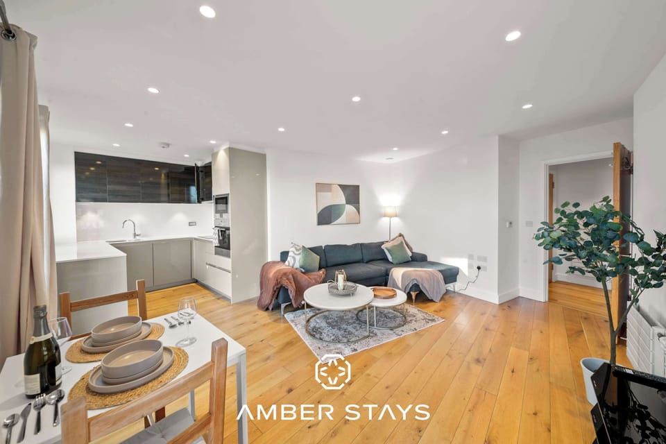 This bright, open-concept apartment features warm wood floors and an integrated living and kitchen space. Modern furnishings, including a dark sofa and round coffee tables, create a clean and inviting atmosphere.