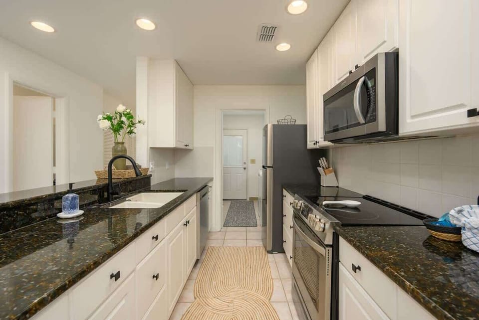 A modern, bright galley kitchen featuring dark granite and white cabinetry.