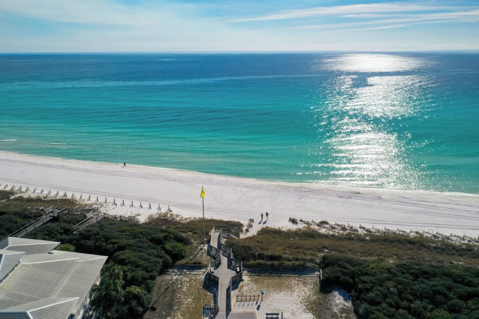 Stunning aerial view showcases pristine white sand beach meeting turquoise waters, with convenient boardwalk access through coastal vegetation.