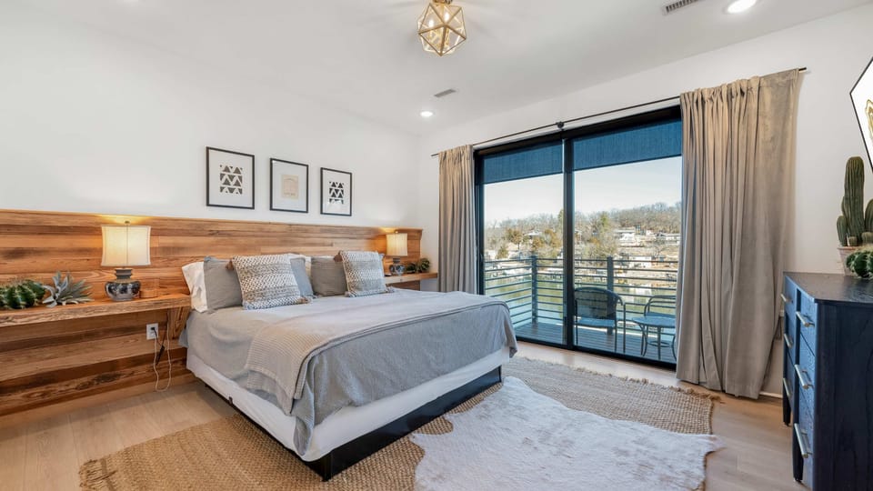 Wake up to beautiful lake views in this inviting bedroom featuring a comfortable bed, warm wood accents, stylish furnishings, and large glass doors opening to the scenic waterfront setting.