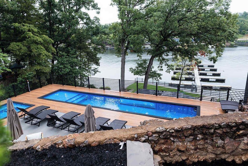 Enjoy a refreshing swim with a view in the lakefront pool area, surrounded by mature trees, natural stone landscaping, and beautiful waterfront scenery.