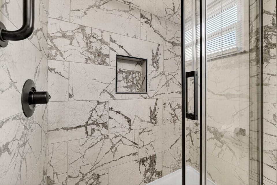 Glass-enclosed shower with marble-look tile and modern fixtures.