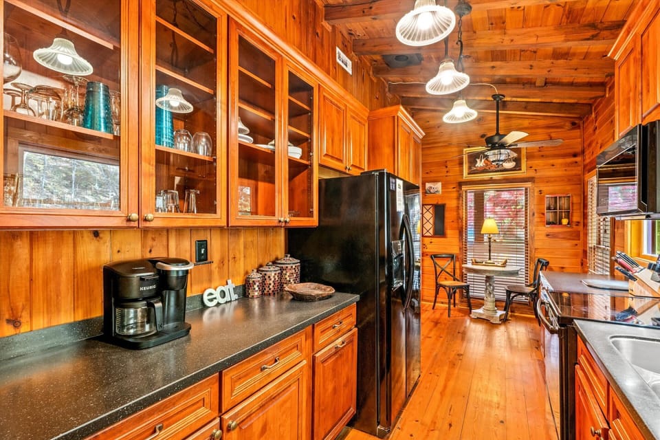 A beautifully appointed kitchen with glass-front cabinets, ample counter space, and cozy lighting leads into a bright breakfast nook overlooking the tranquil forest.