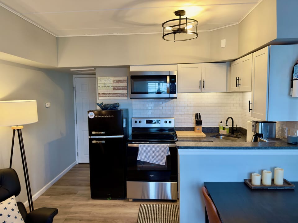 Inviting kitchen area with stainless steel appliances, electric range, farmhouse sink and white subway tile backsplash. Features a cozy breakfast bar with candles and stylish pendant lighting for a warm culinary experience.