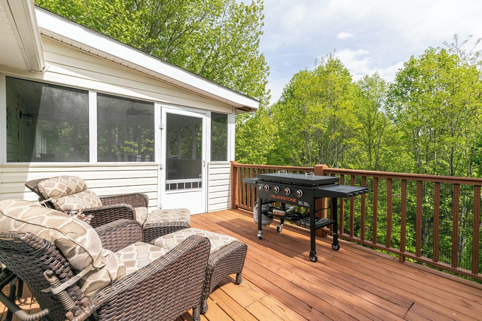 Sunny deck at Our Happy Nest with comfy seating and a flat-top grill, surrounded by lush Blue Ridge trees.