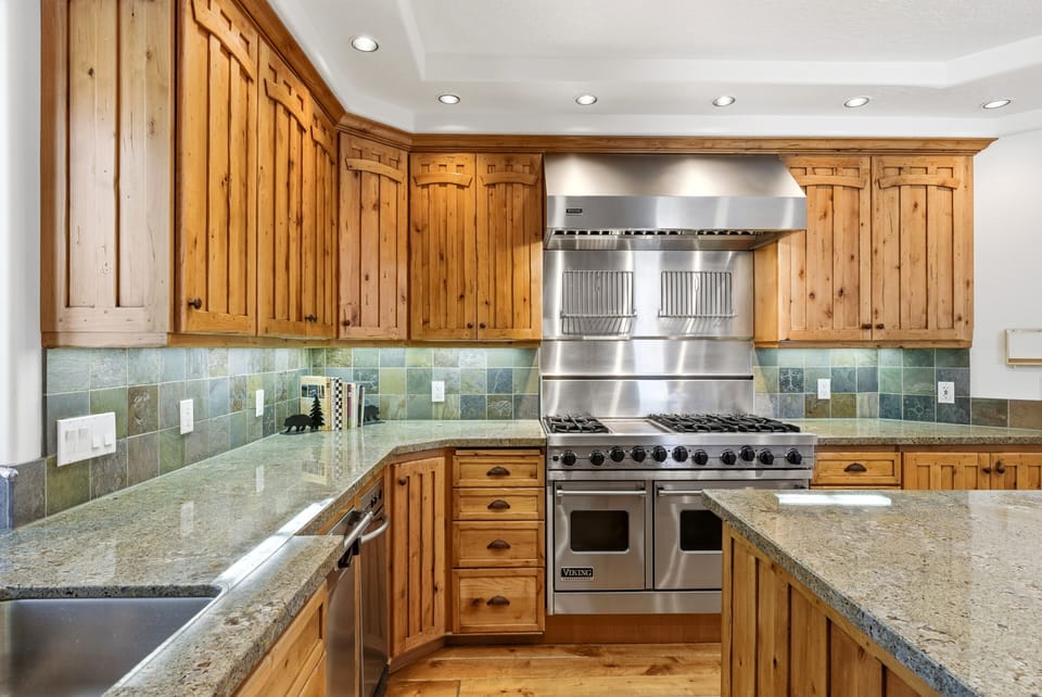Compact gourmet kitchen with granite counters, stainless steel range and hood, and wood cabinetry offering a cozy, functional layout.