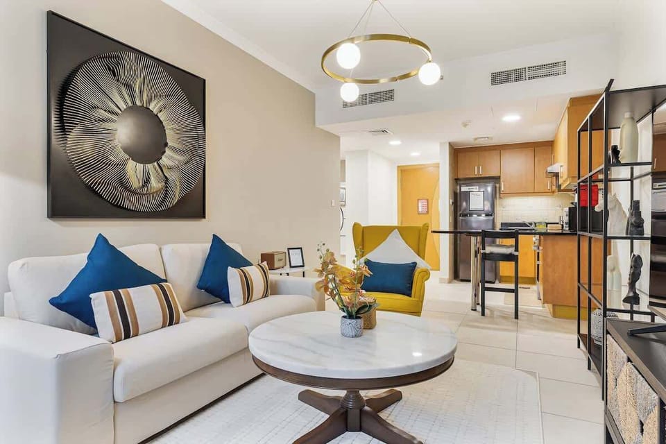 Bright and inviting living room featuring a cozy sitting area, and a 65-inch TV, while the open kitchen seamlessly connects to the living area in the background, creating a spacious and welcoming layout.