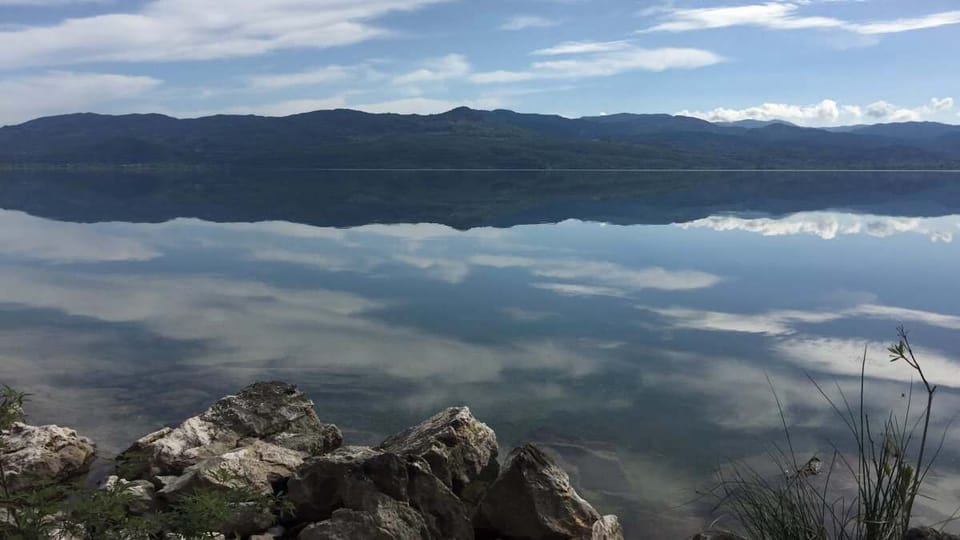 Mirror-like waters and mountain reflections at Lake Trichonida, an ideal spot for relaxation, photography, and quiet moments in nature.
