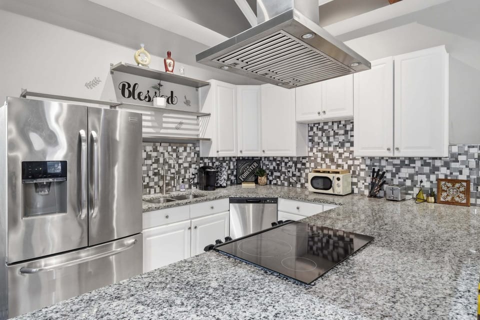 Full kitchen with white cabinets, granite counters, mosaic backsplash, and stainless-steel appliances.