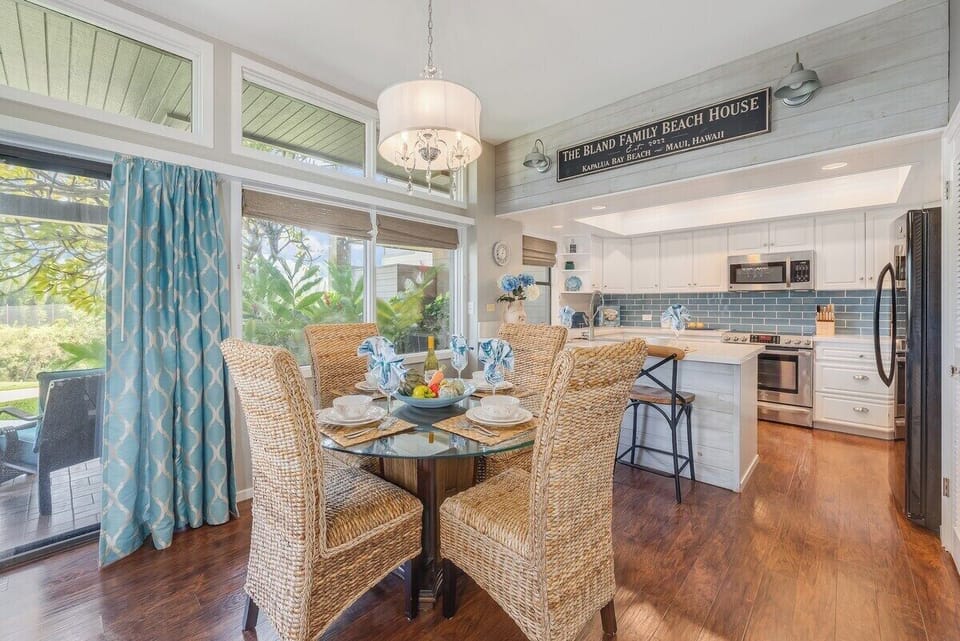 Dine in a stylish setting with a round glass-top table and woven chairs, framed by large windows and vibrant blue drapery.