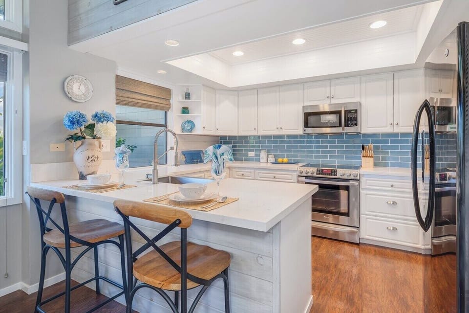 Cook and entertain in a modern kitchen with white cabinetry, stainless steel appliances, and a spacious island accented by blue tile backsplash.