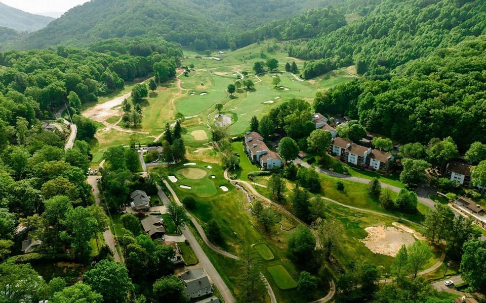 Aerial view of rolling golf greens tucked in mountain forest