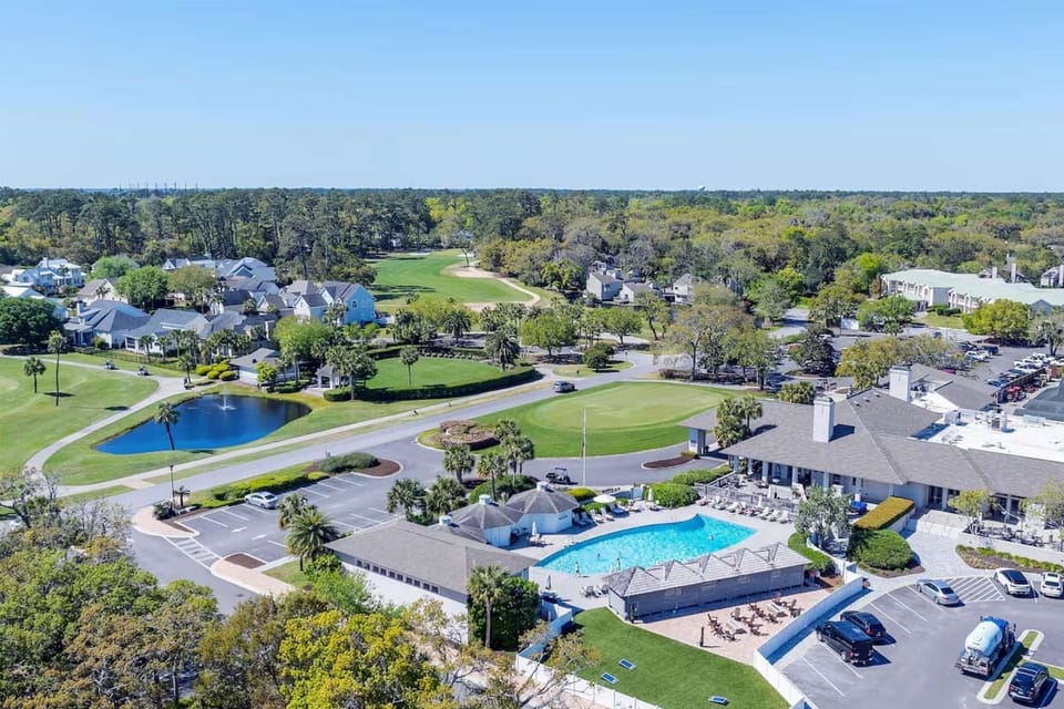 Wide aerial of pool, clubhouse, golf course, and nearby homes