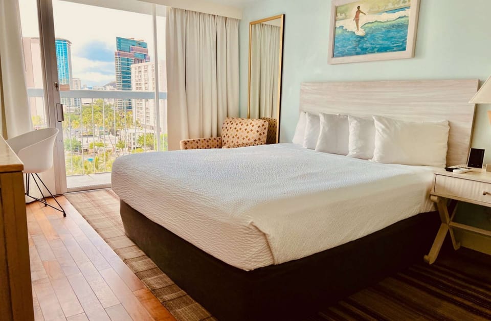 King bed beside tall windows showing city buildings and trees