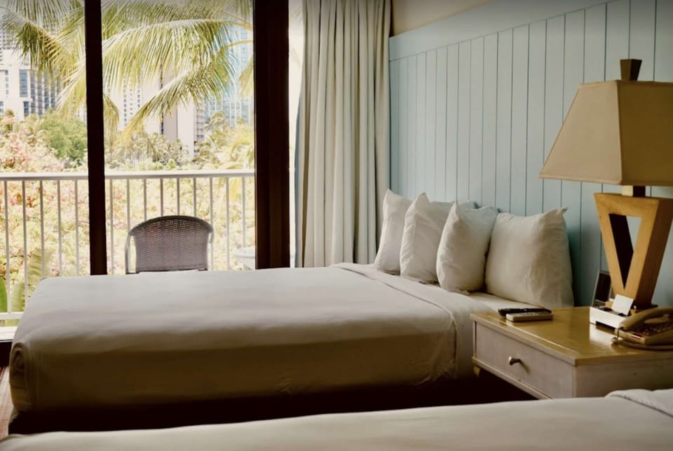 Bright room with two beds facing a balcony with palm trees outside