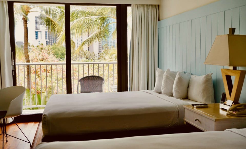 Room with two beds and balcony view of palm trees and city