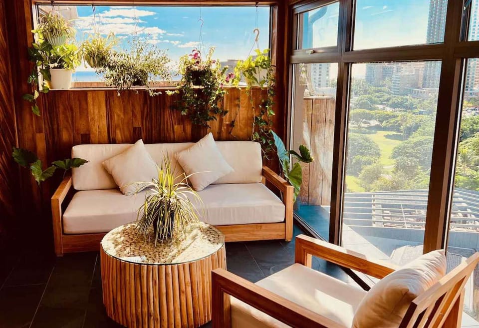 Cozy lounge with sofa, plants, and sunny window views of the city